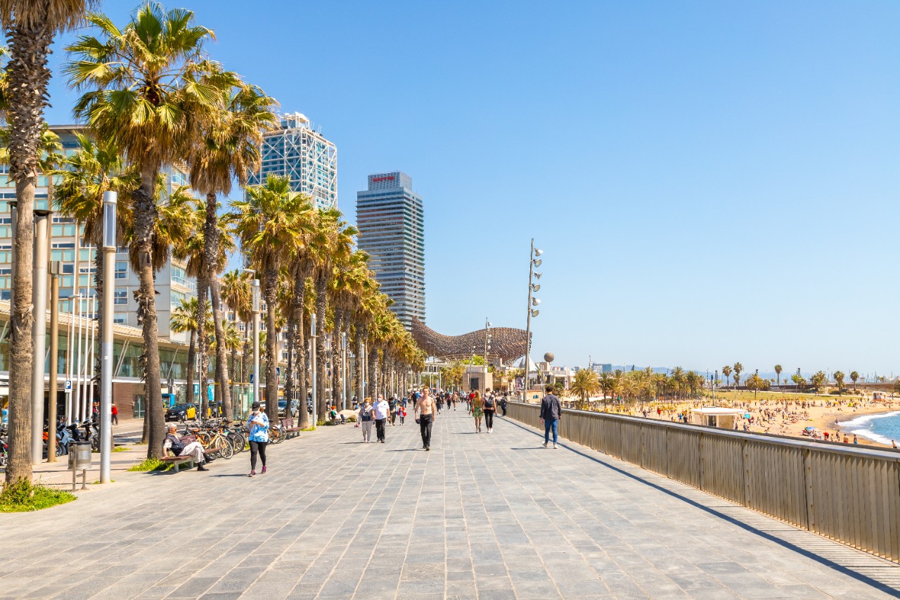 Spaziergänger auf der Strandpromenade in Barceloneta bei Sonnenschein.