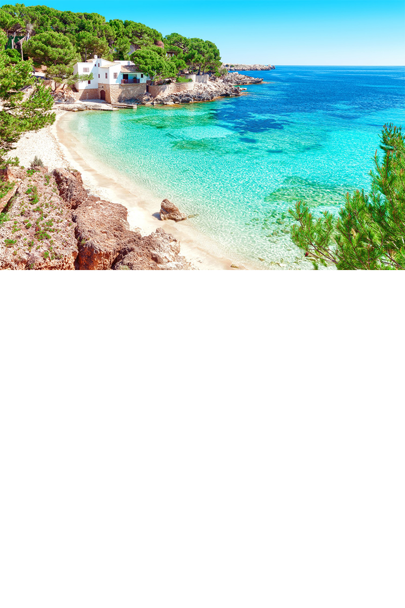 Türkisblaues Wasser und weißer Sandstrand auf Mallorca, eingerahmt von Bäumen und einem weißen Haus 
