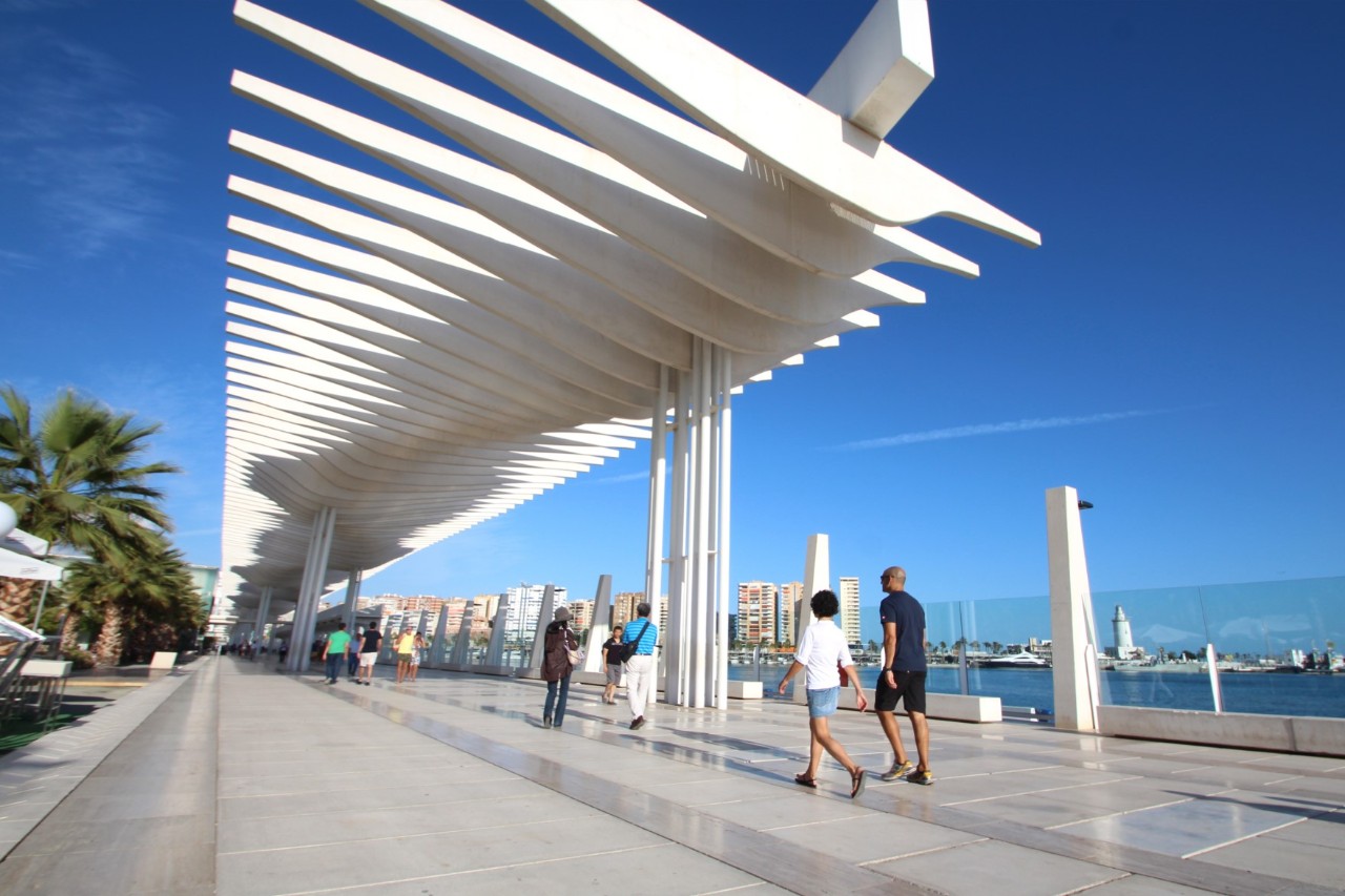 Moderne Hafenpromenade mit weißen Säulen, Palmen und Spaziergängern.