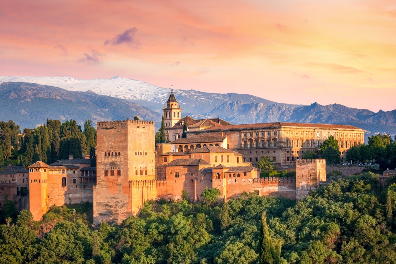 Alhambra mit Palastmauern und Türmen vor grünen Hügeln in Granada.