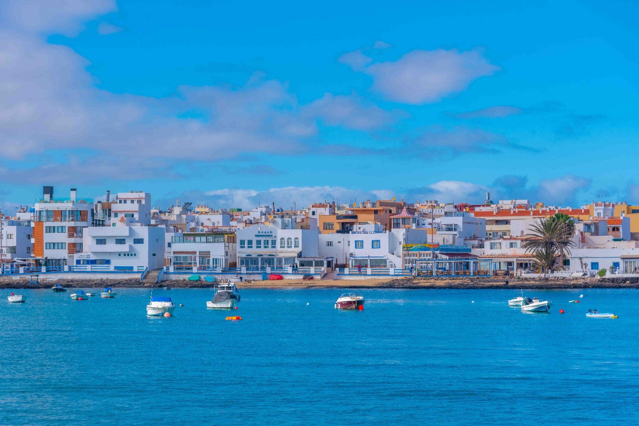 Häuser in Corralejo vom Wasser aus mit blauem Himmel im Hintergrund.