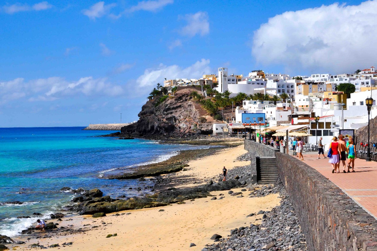 Weiße Häuser, Promenade und Strand in Morro Jable bei Sonnenschein.