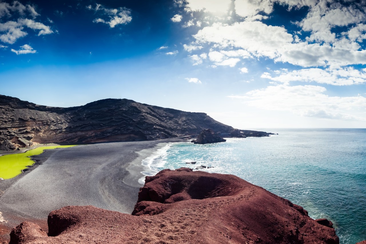 Dunkler Sandstrand mit türkisfarbenem Meer und sanften Wellen auf Lanzarote.