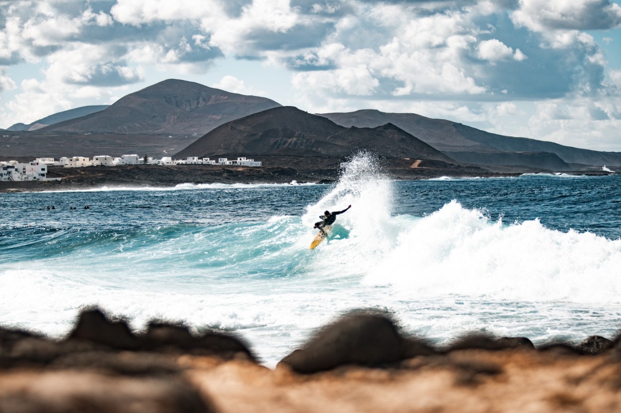 Küstenabschnitt in La Santa mit Felsen, Wellen und weißen Häusern auf Lanzarote.