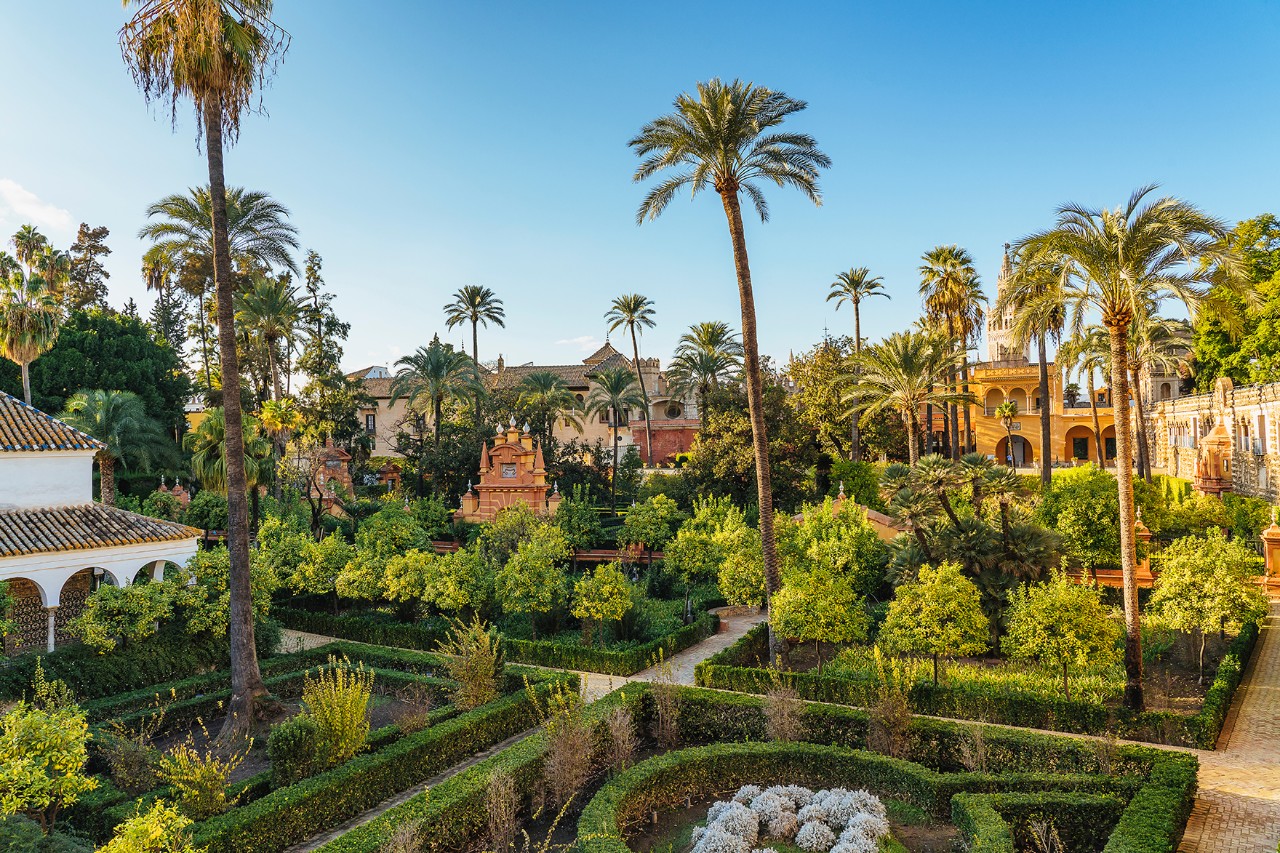 Üppige Gartenanlage mit Palmen, Ziersträuchern und historischen Bauwerken.