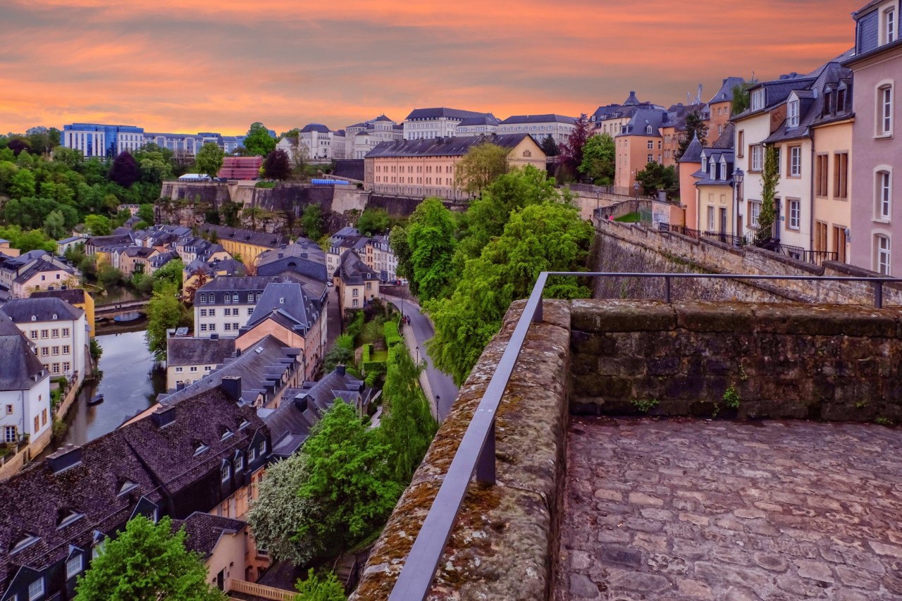 Gepflasterter Weg mit Ausblick auf die Stadt Luxemburg, den Fluss, Dächer und Bäume in der Dämmerung 