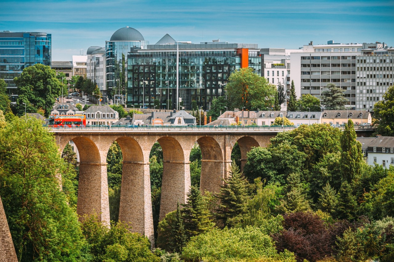 Viadukt mit grünen Bäumen im Vordergrund und modernen Gebäuden im Hintergrund 