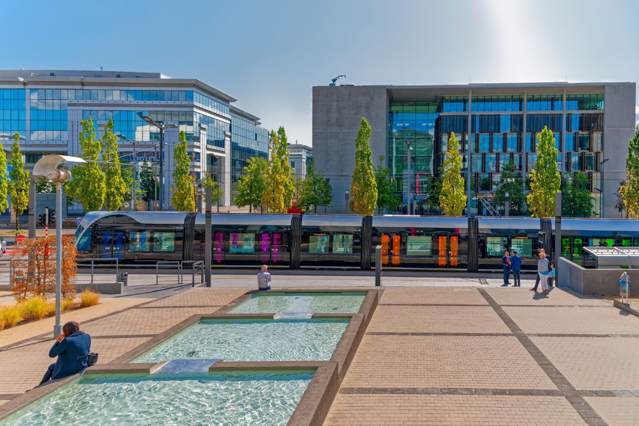 Platz mit modernen Häusern mit Glasfassade, Straßenbahn und Springbrunnen 