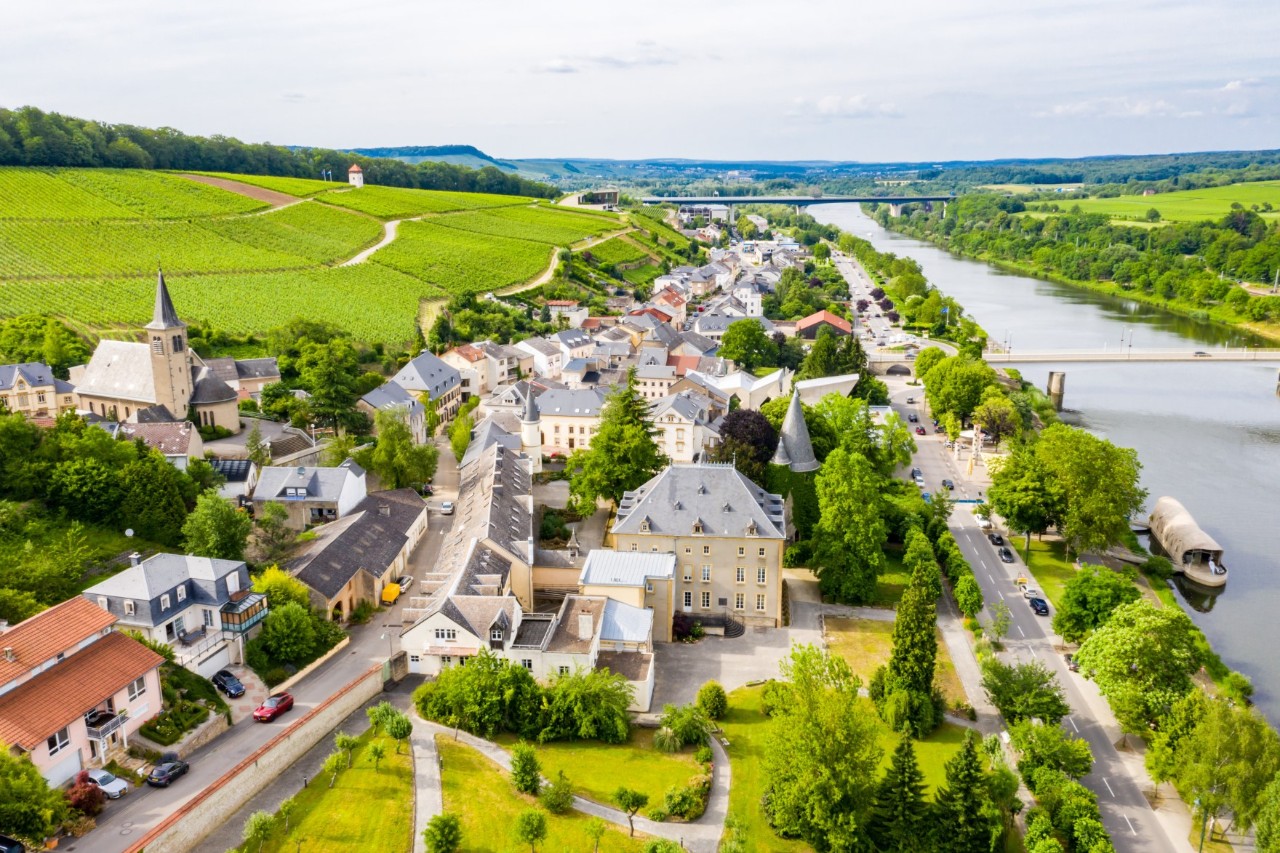 Das Dorf Schengen linksseitig vom Fluss Mosel, umgeben von saftigen, grünen Wiesen. 