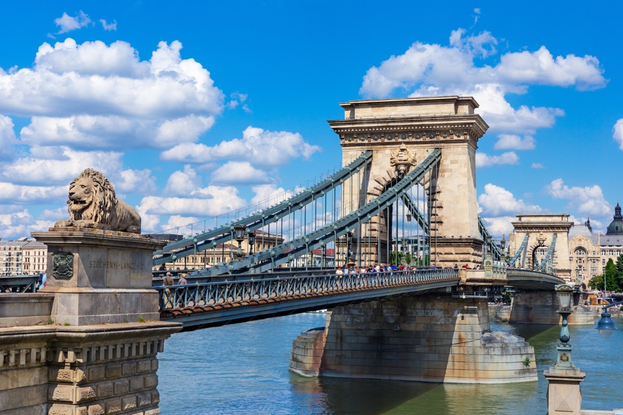 Kettenbrücke mit Löwenstatue und Fußgängern über der Donau.