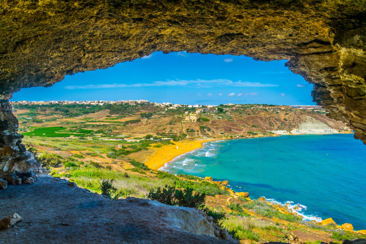 Blick aus Höhle auf den rötlich-goldenen Sandstrand der Ramla Bay auf Gozo.
