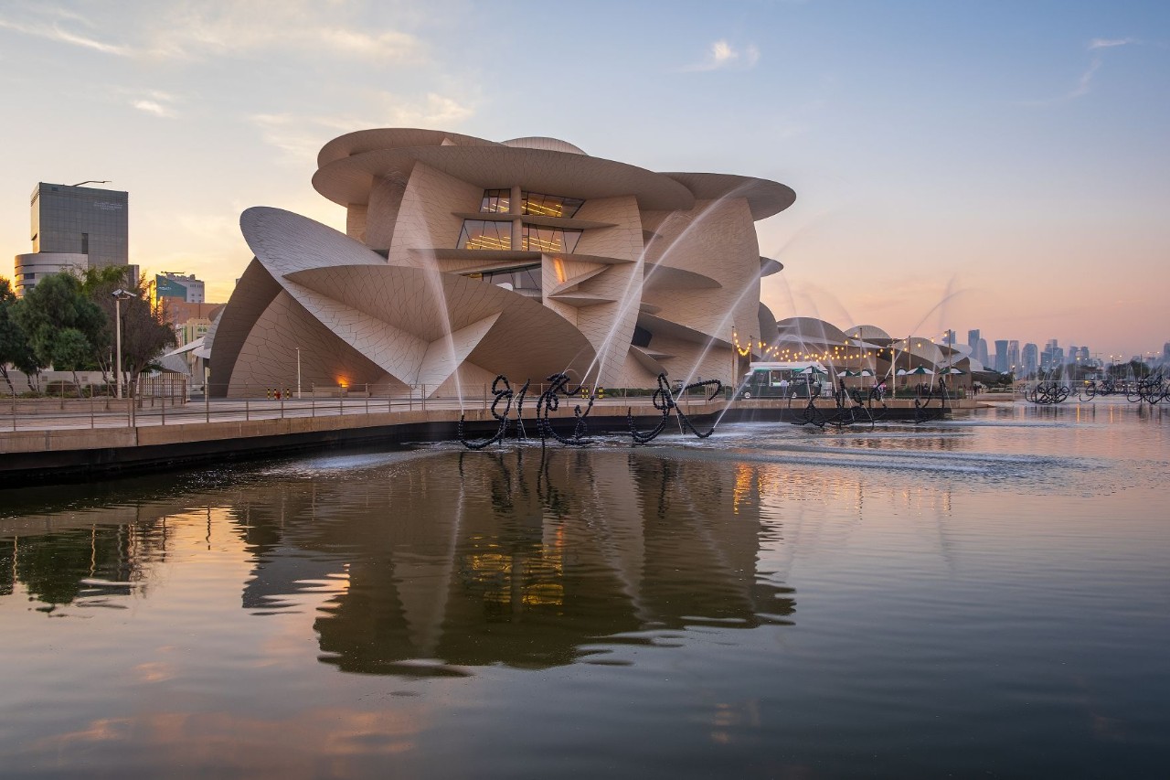 Nationalmuseum von Katar mit Spiegelung im Wasser bei Abendlicht.