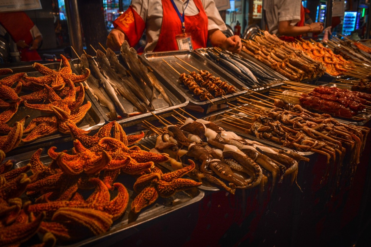 Straßenstand in Peking mit gegrillten Snacks und dampfenden Speisen.