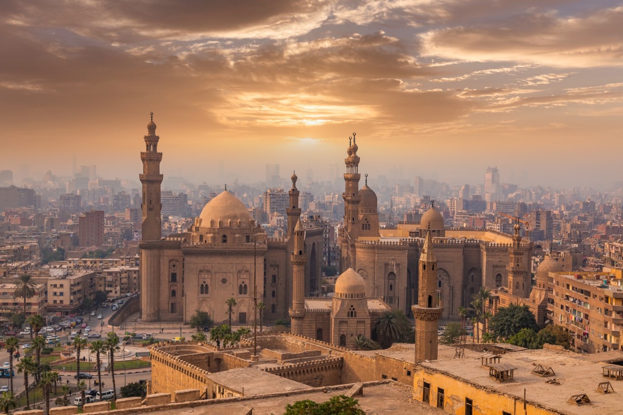Panoramablick auf Kairos Altstadt mit der Sultan-Hassan- und Al-Rifa'i-Moschee bei Sonnenuntergang.
