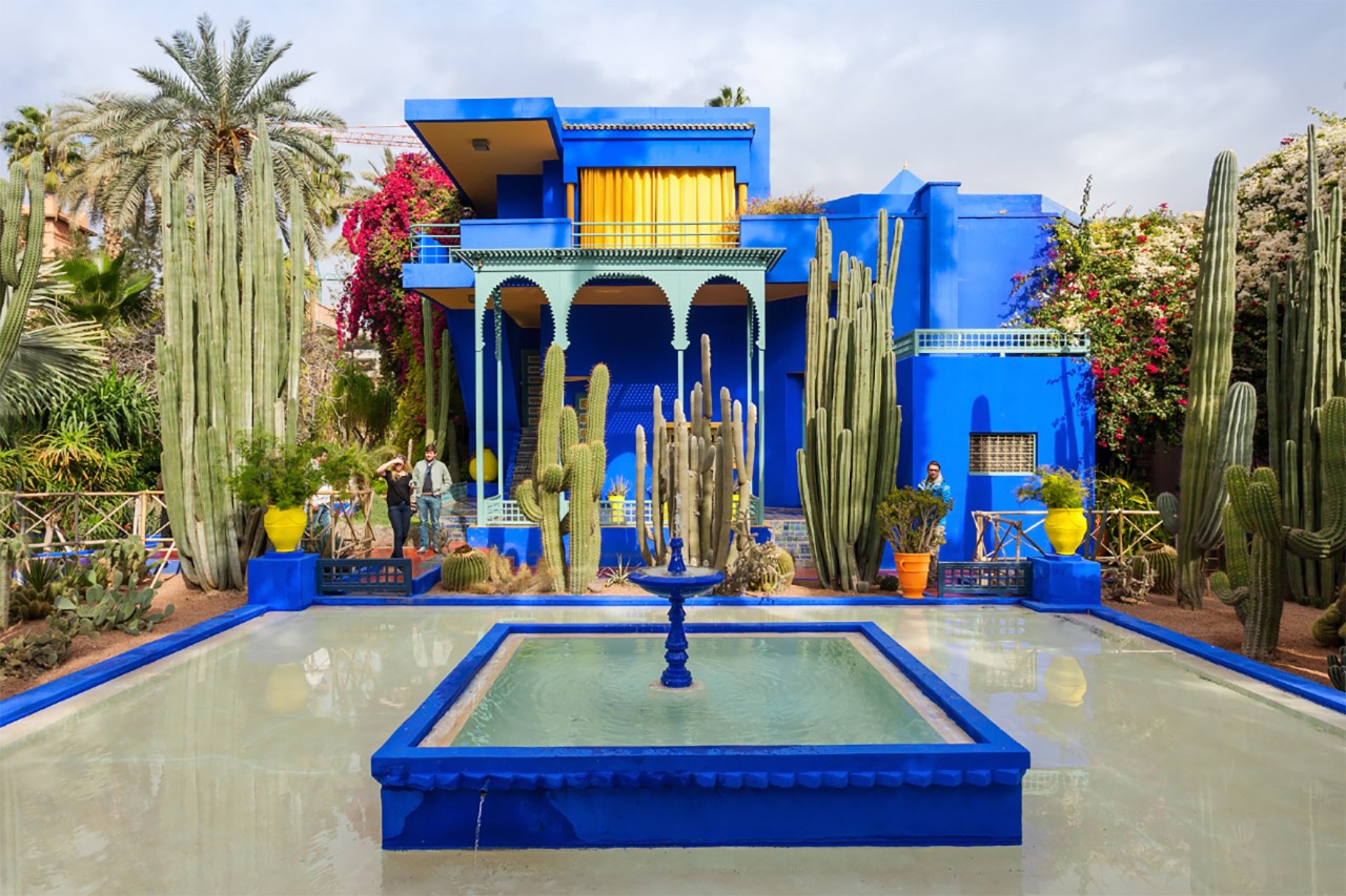 Kobaltblaues Gebäude im Jardin Majorelle mit Palmen und Kakteen.