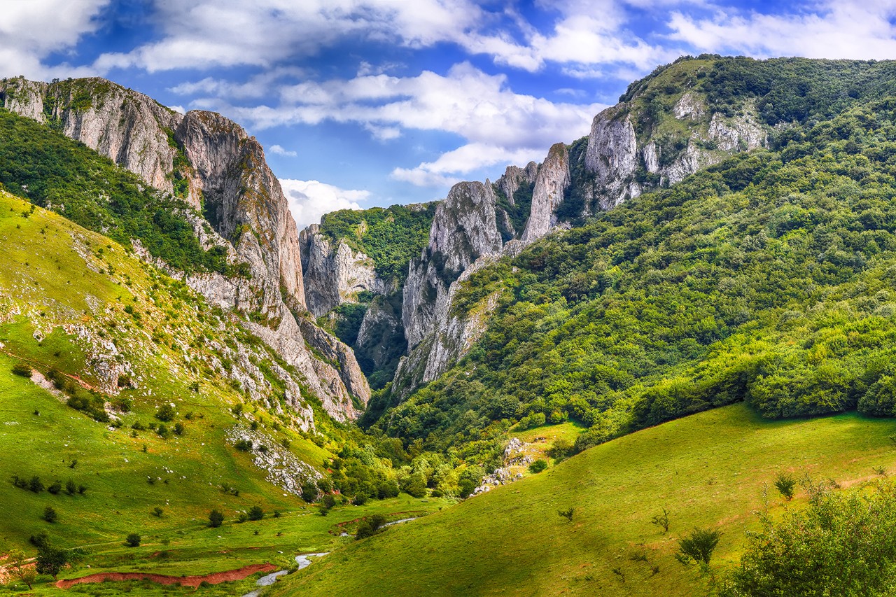 Das Bild zeigt eine Schlucht zwischen grünen Bergen und grauen Felswänden.