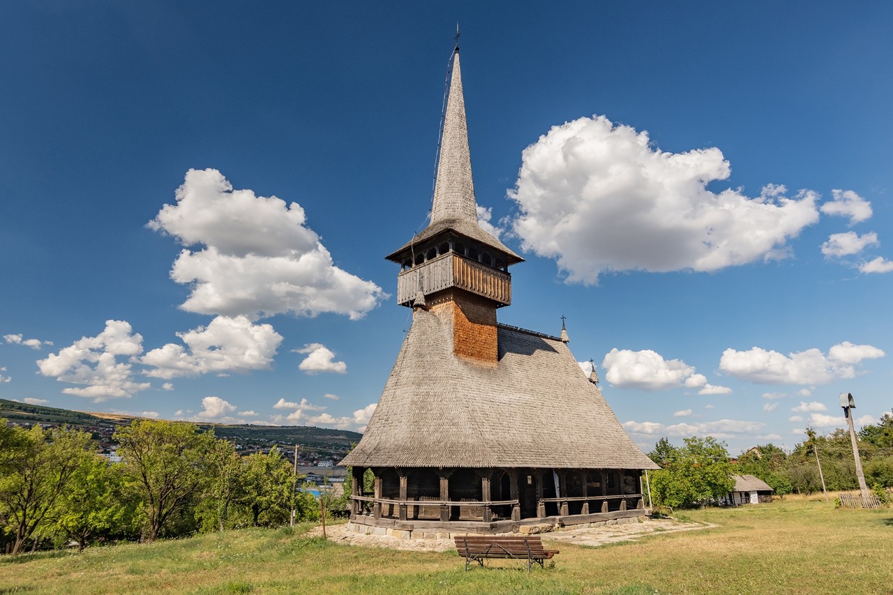 Das Bild zeigt eine alte Holzkirche auf einer Wiese vor blauem Himmel.