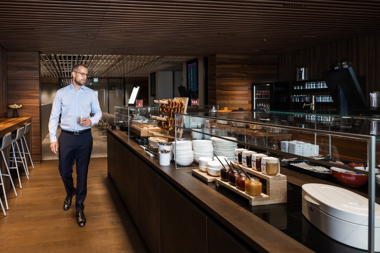 Ein Mann im Anzug, um die 40 Jahre alt, läuft entlang eines Buffets. Gemütliches Ambiente durch Beleuchtung.