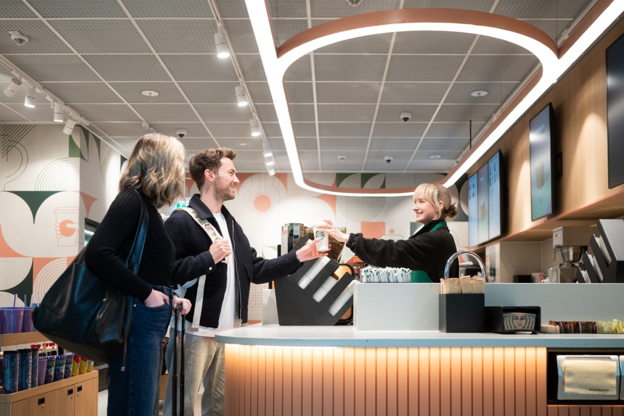 2 Personen bestellen bei Starbucks, Mitarbeiterin übergibt Starbucks Becher