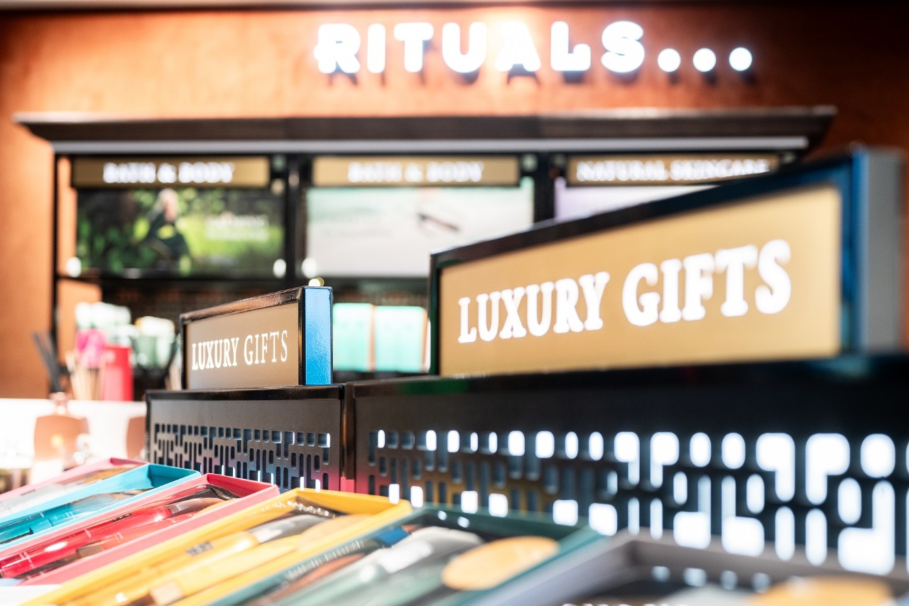 Im Vordergrund eine Kleiderstand mit der Aufschrift "Luxury Gifts": Dahinter eine Wand mit der Aufschrift "Rituals" in braun gehalten.