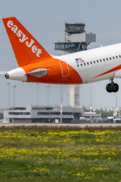 Heck eines easyJet-Flugzeugs kurz nach dem Start. Im Hintergrund sind eine Wiese und der Tower des BER zu sehen.