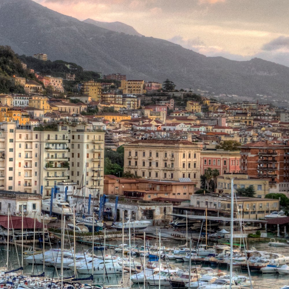 Blick auf die Altstadt von Salerno. Viele Häuse.r Davor der Hafen mit Booten.