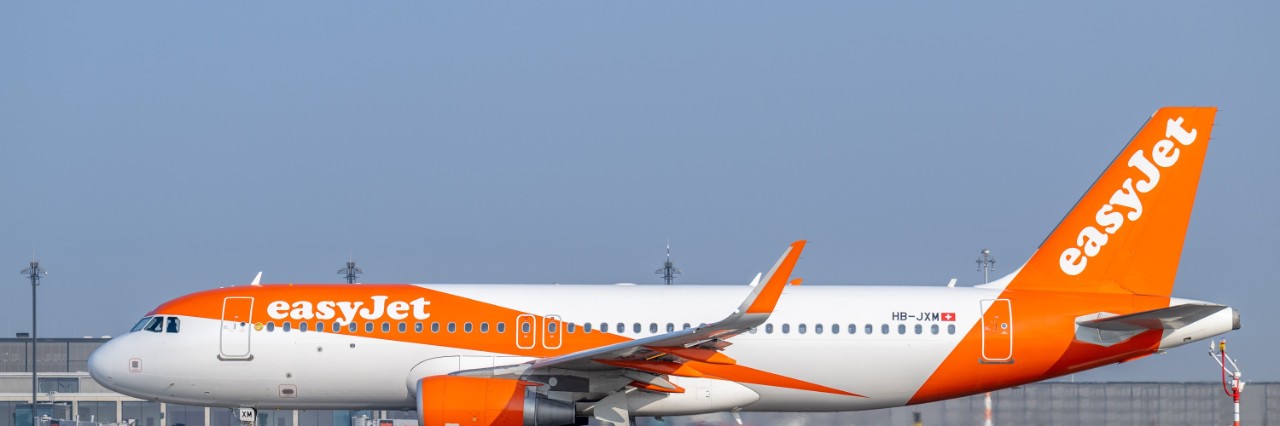 Heck eines Eurowings-Flugzeugs vor dem Schriftzug "Berlin Brandenburg Airport Willy Brandt" an der luftseitigen Fassade des Terminal 1 des BER