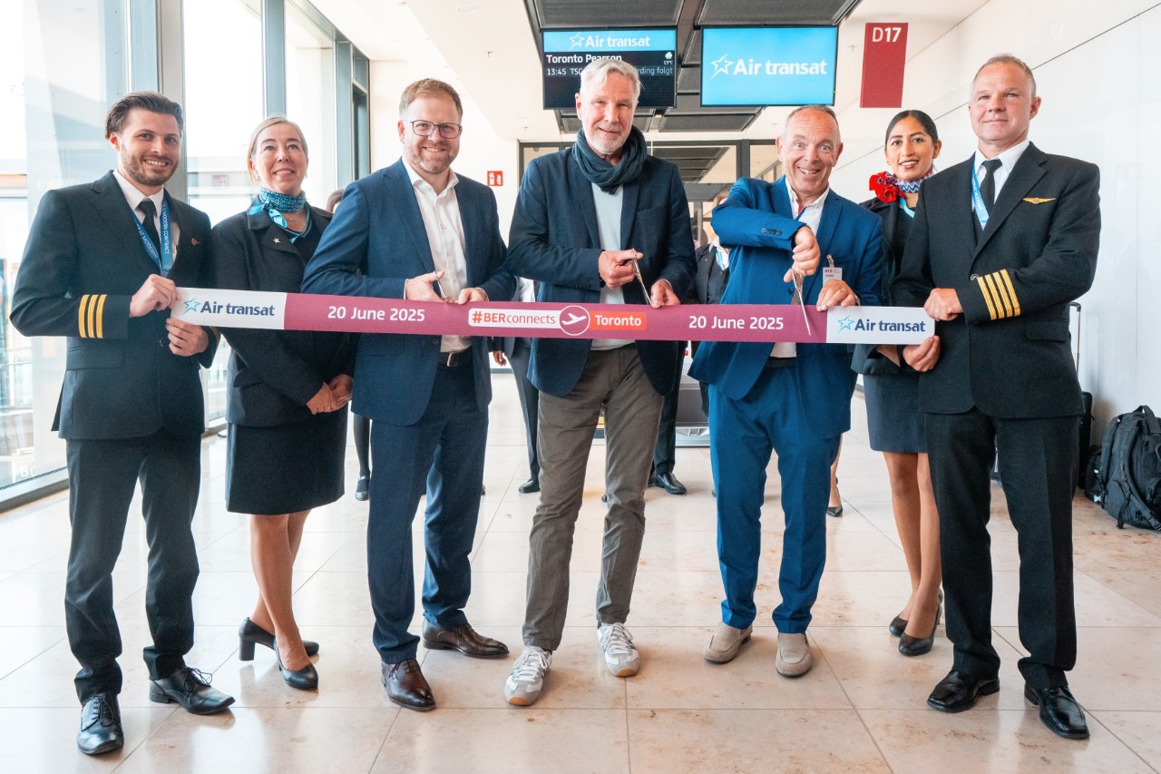 Eine Gruppe Menschen steht am Gate im Terminal und hält ein Band in den Händen