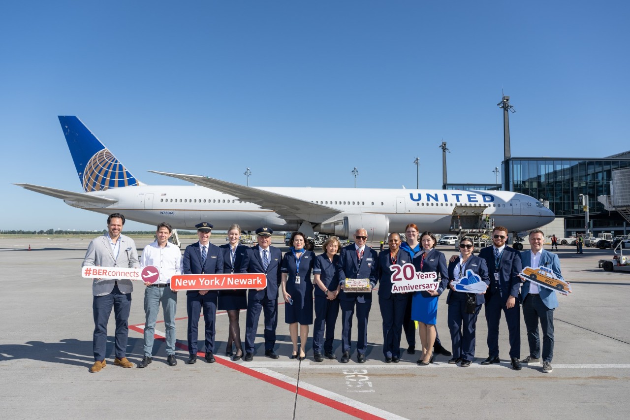 Eine große Gruppe Menschen posiert vor einem Flugzeug auf dem Vorfeld. Teilweise halten sie Schilder mit Aufschriften in den Händen. Einige von ihnen tragen die Uniformen einer Flugzeug-Crew. 