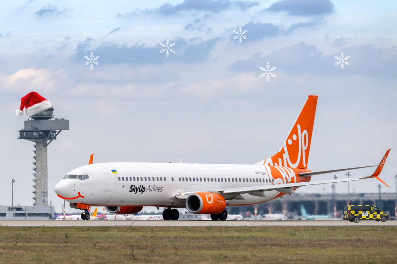 Ein Flugzeug der Airline SkyUp auf einem Vorfeld mit Schneeflocken und Weihnachtsmütze auf dem Tower