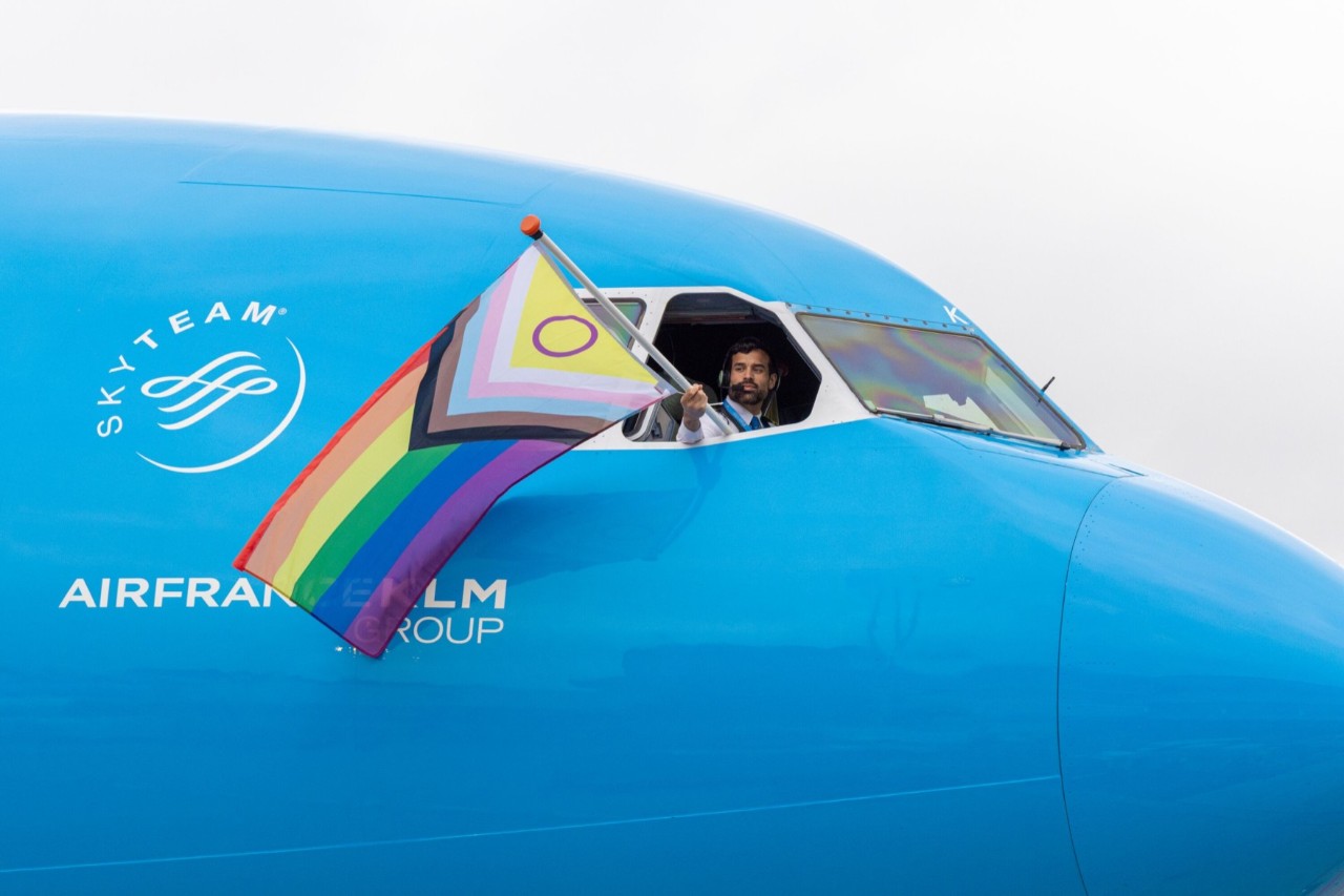 Ein Pilot schwenkt aus dem Cockpit-Fenster eines KLM-Flugzeugs eine Pride-Flagge