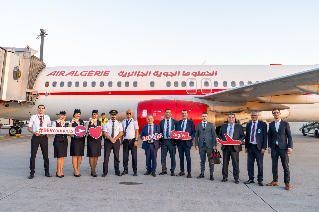 Eine Gruppe von Menschen, die mit Schildern auf dem Vorfeld des BER vor einem Flugzeug der Air Algérie posieren