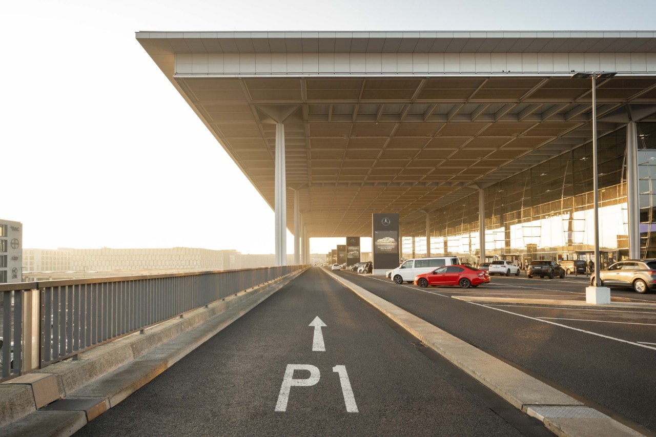 Straße mit Aufschrift P1 führt unter dem Terminaldach hindurch. Autos stehen auf dem Kurzzeitparkplatz.