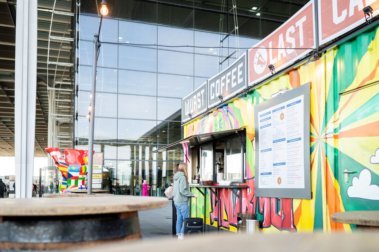 The Last Call Bar in front of BER Terminal 1. The bar is colorful. The glass facade of the terminal in the background.