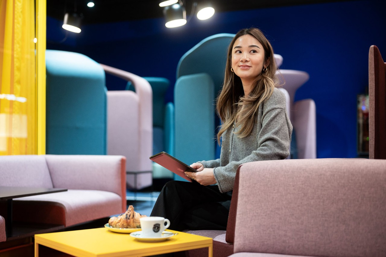 Woman sitting on armchair in Nuuuork. In front of her a cup of coffee and a croissant.