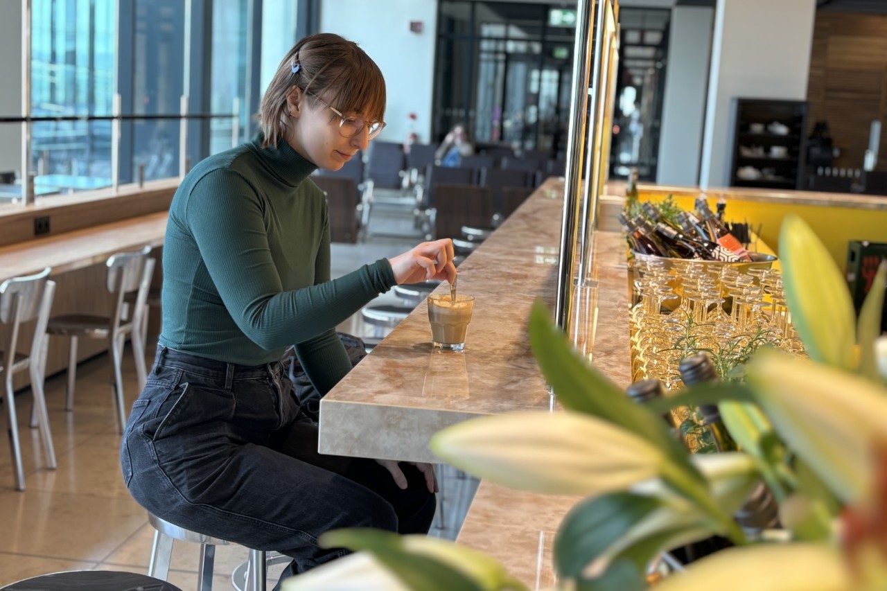 A young woman sitting at a bar, drinking coffee