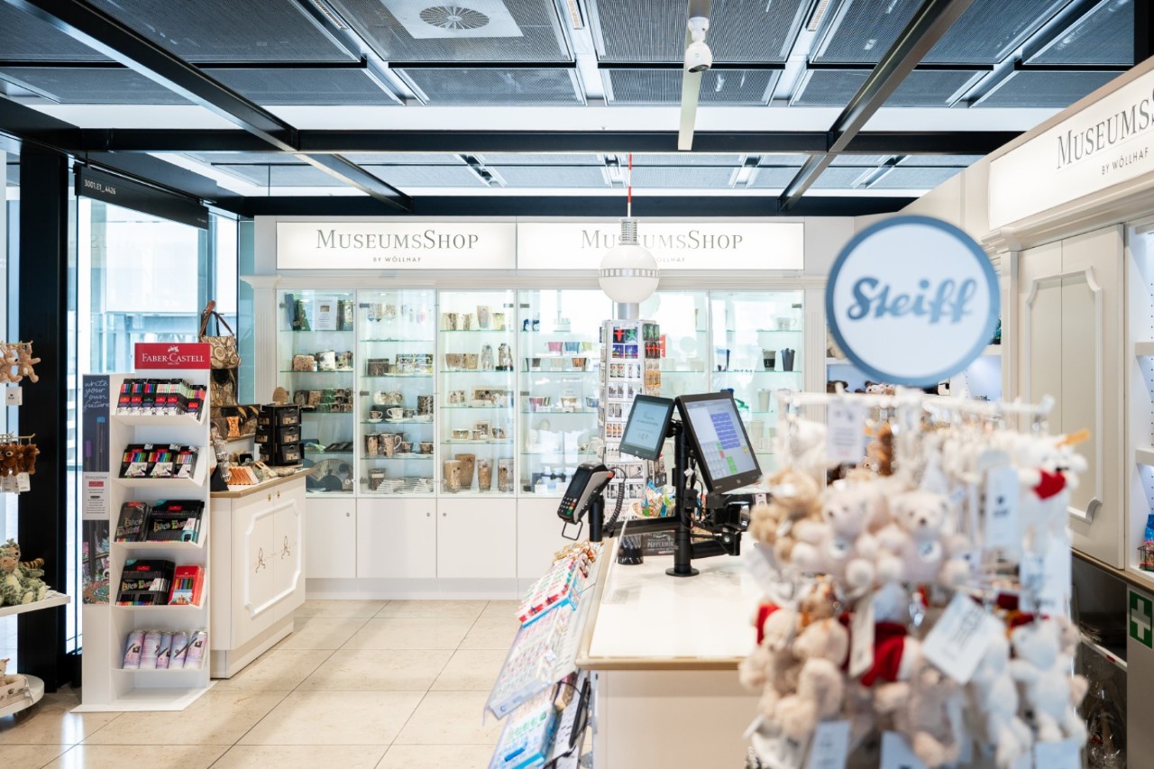 Numerous counters with display in the MusseumsShop store. Wall shelves in the background.