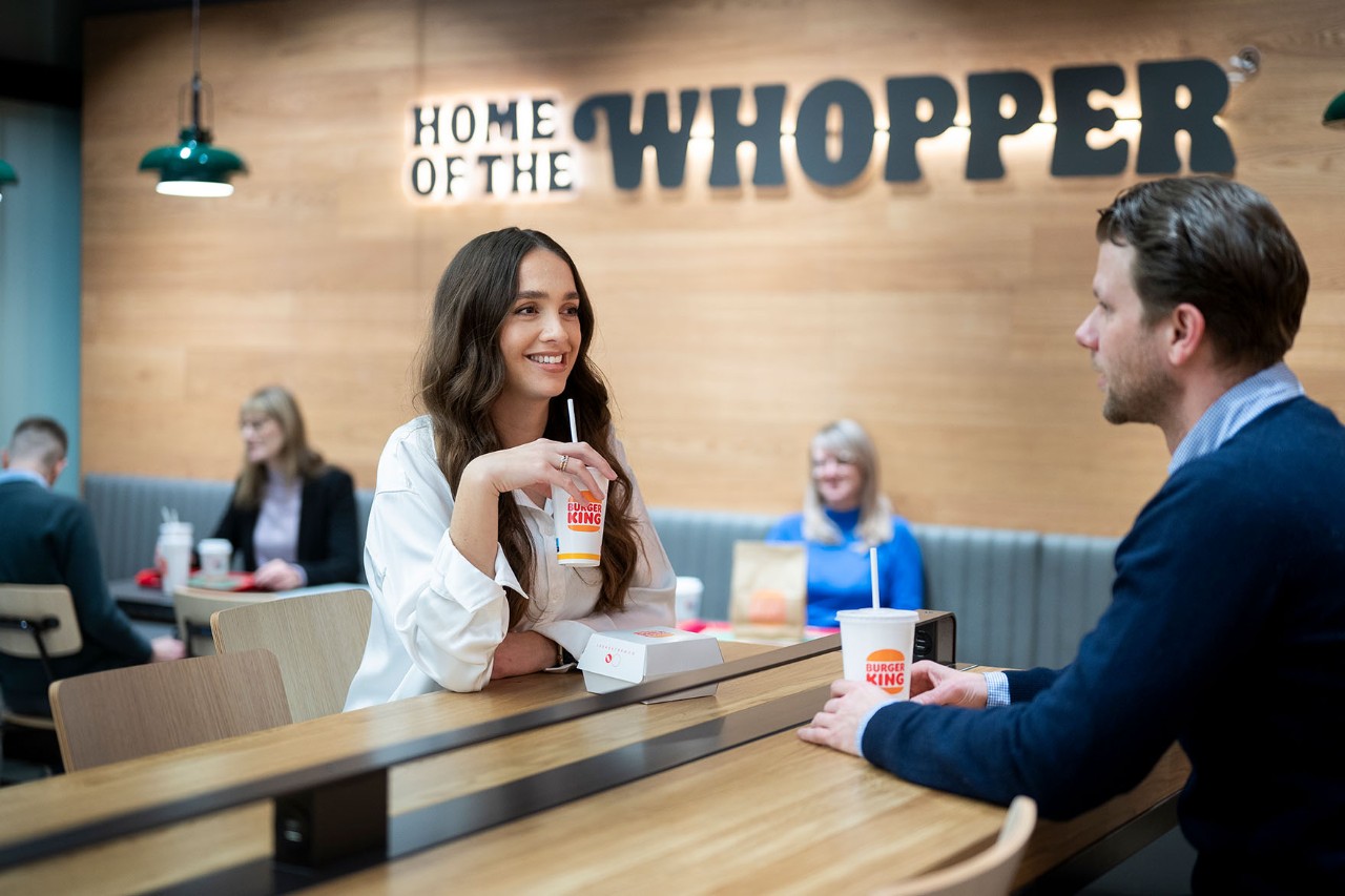 A man and a woman are sitting in the Burger King with drinks in their hands.