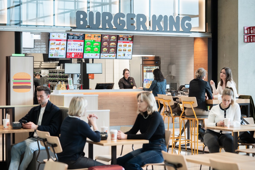 Several people in the seating area of the Burger King. Behind them the counter and the offer on displays.