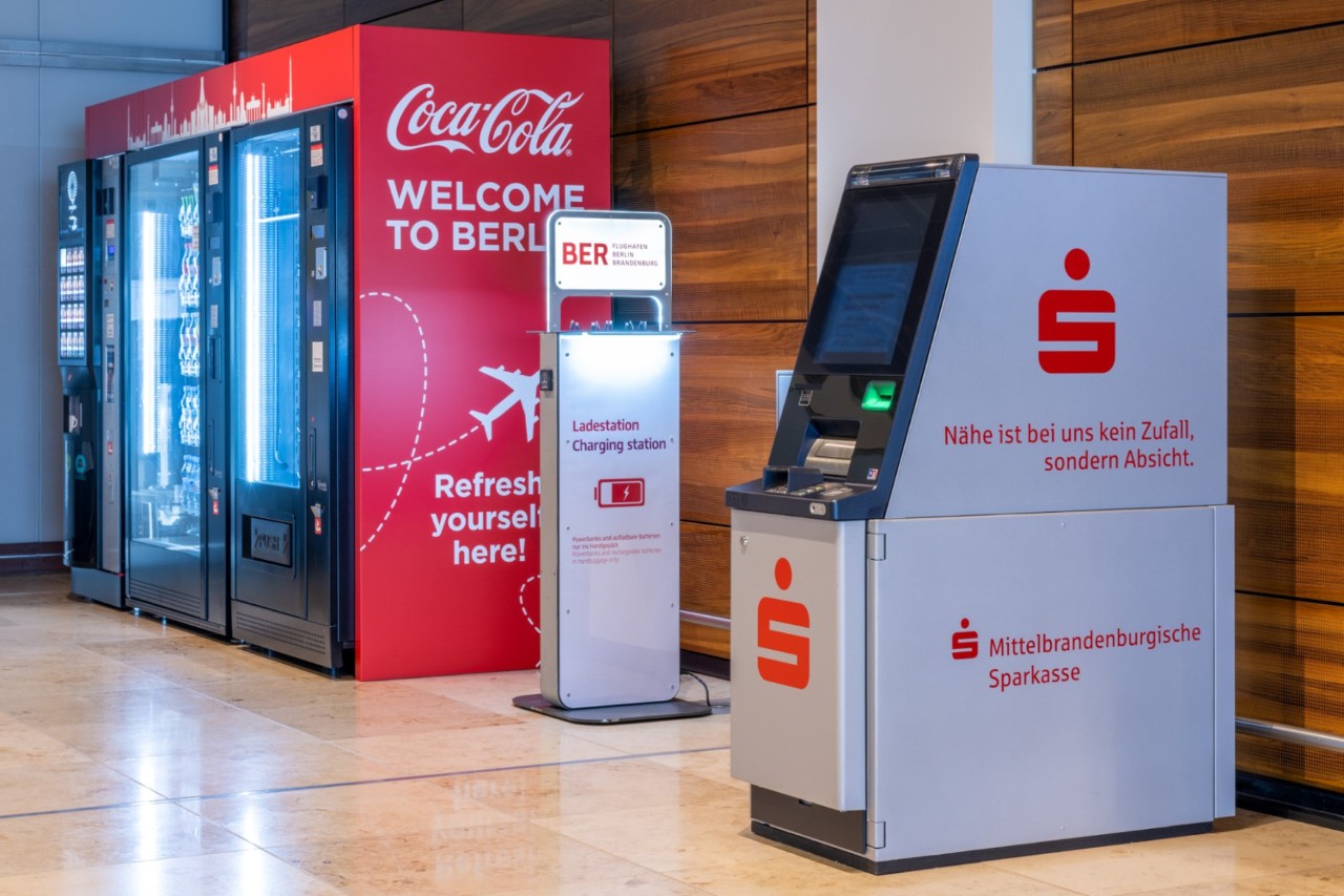 Sparkasse ATM in the foreground. Behind it is a charging station for cell phones and a drinks machine.