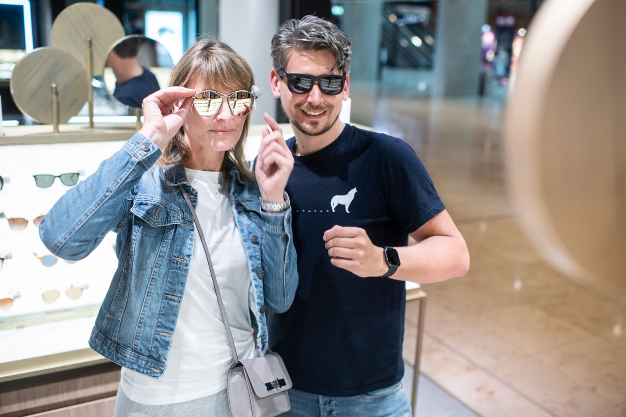 A man and a woman try on sunglasses.