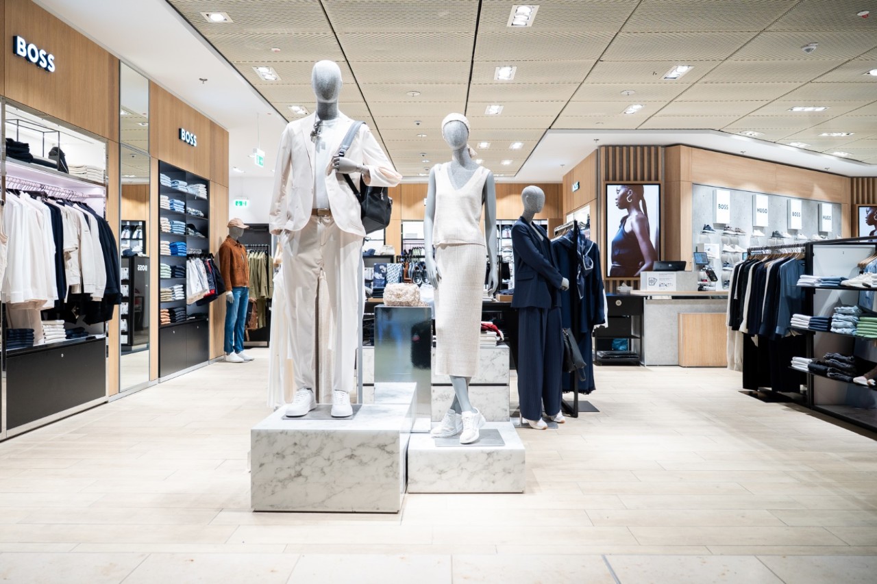 Mannequins wearing white clothing. Behind them are Boss shelves with suits and other clothing items.