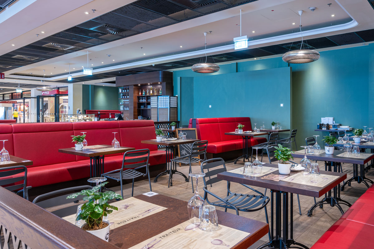 Seating area. Red upholstered benches. Plants on the tables. The bar in the background.