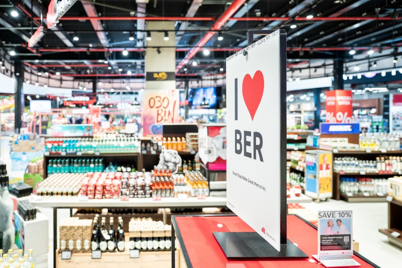 Shelves with goods in the duty-free shop. A display stand with the inscription ‘I love BER’.