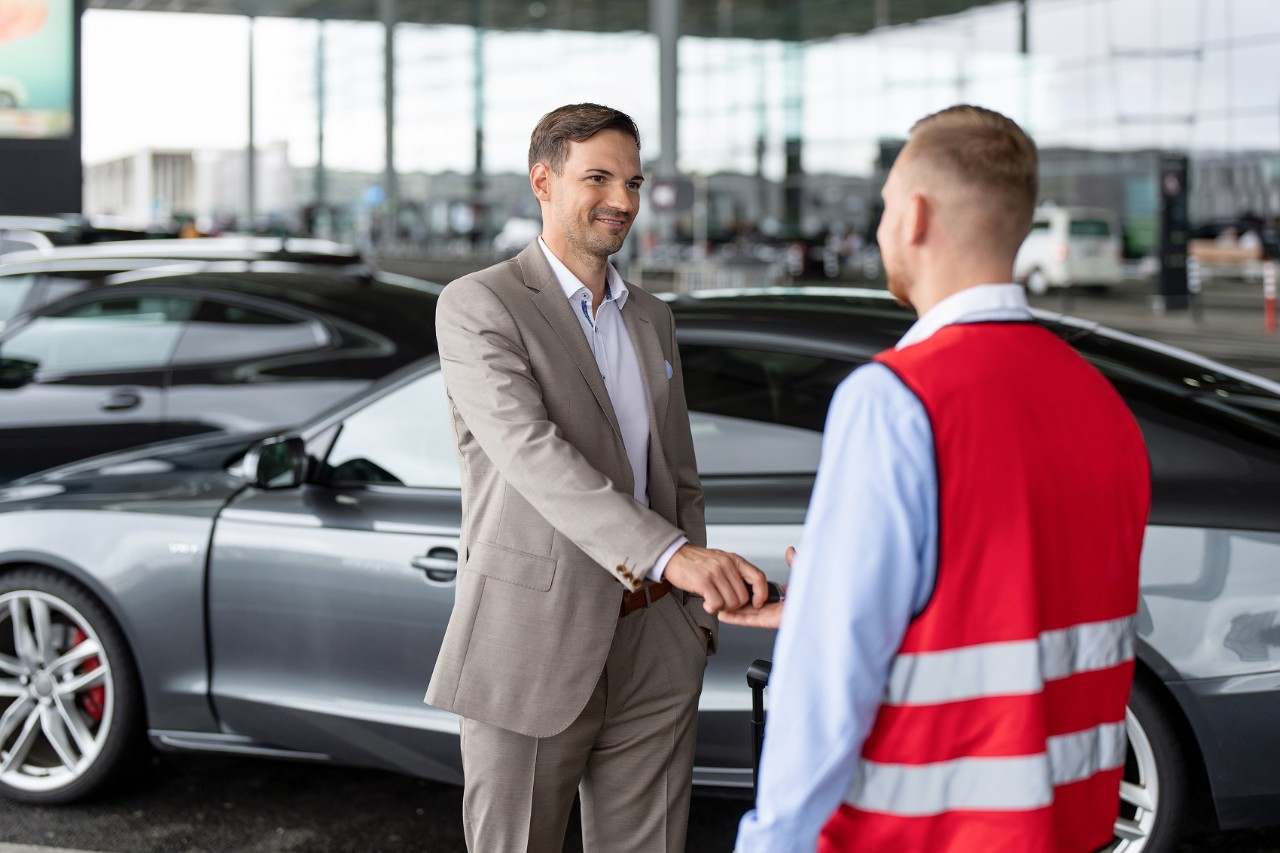 A customer hands the keys to his vehicle to a valet parking employee wearing a vest.