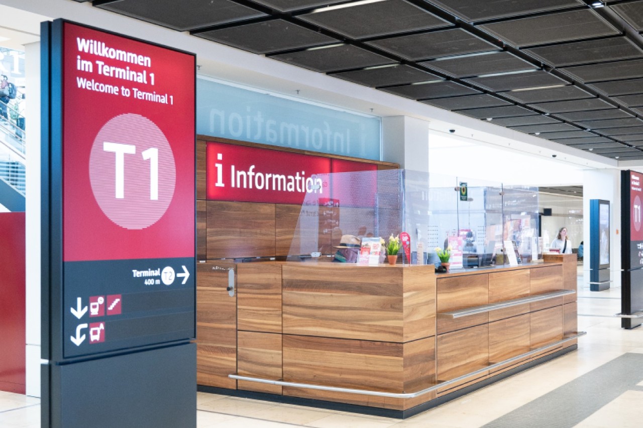 View of the airport information desk from afar. To the left is a stele with the inscription T1.