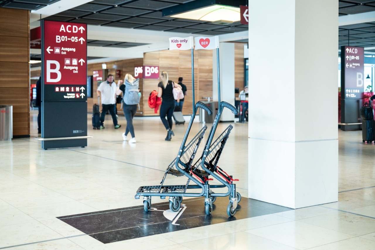 View of numerous buggies in gate area B. Behind them, people in the aisle.