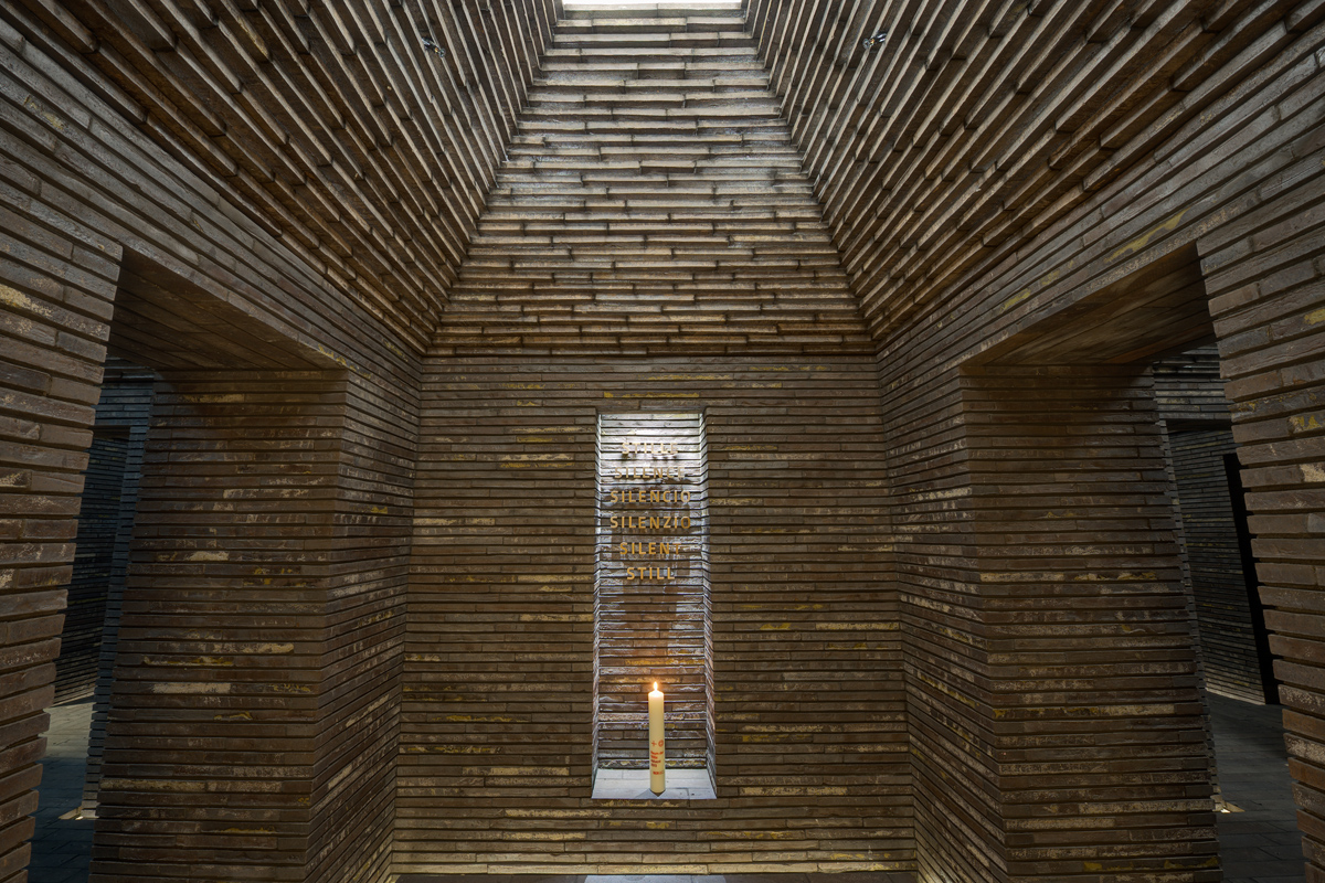 Interior shot of the Still room. Light shines into the room above. There is a candle at the back. The walls are made of brownish stone.