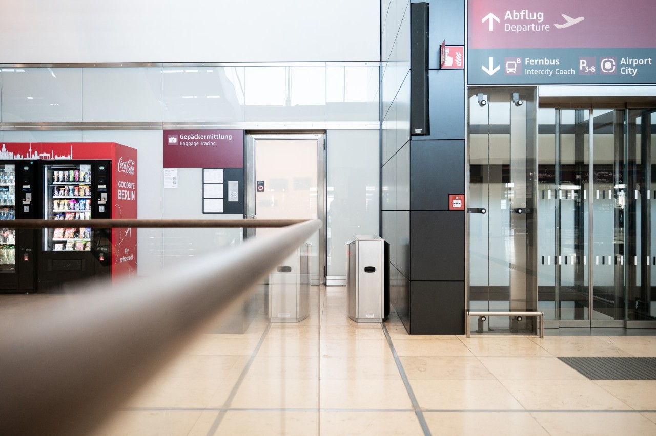 Door in frosted glass with the sign “Gepäckermittlung”. An elevator on the right. A drinks machine on the left.