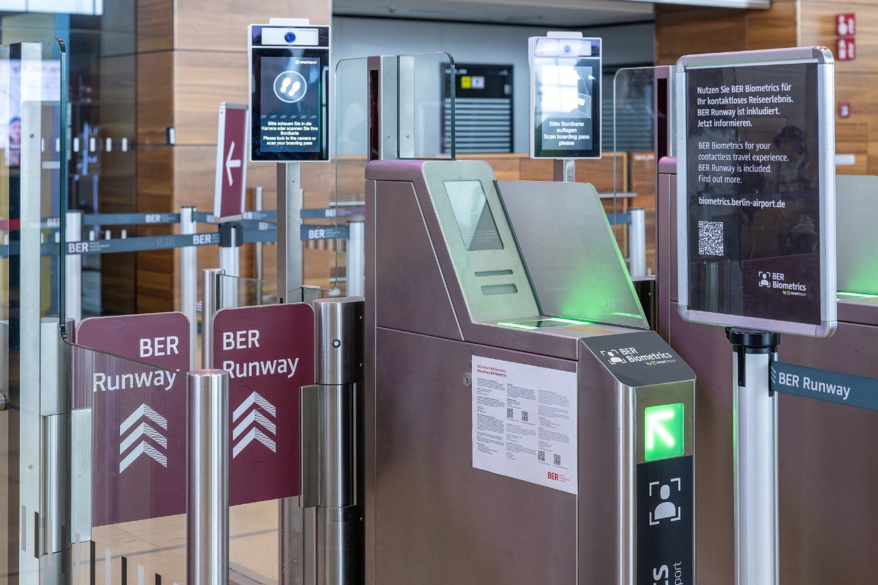 People with suitcases standing in front of a flight information display. One of the screens shows information about BER Runway.
